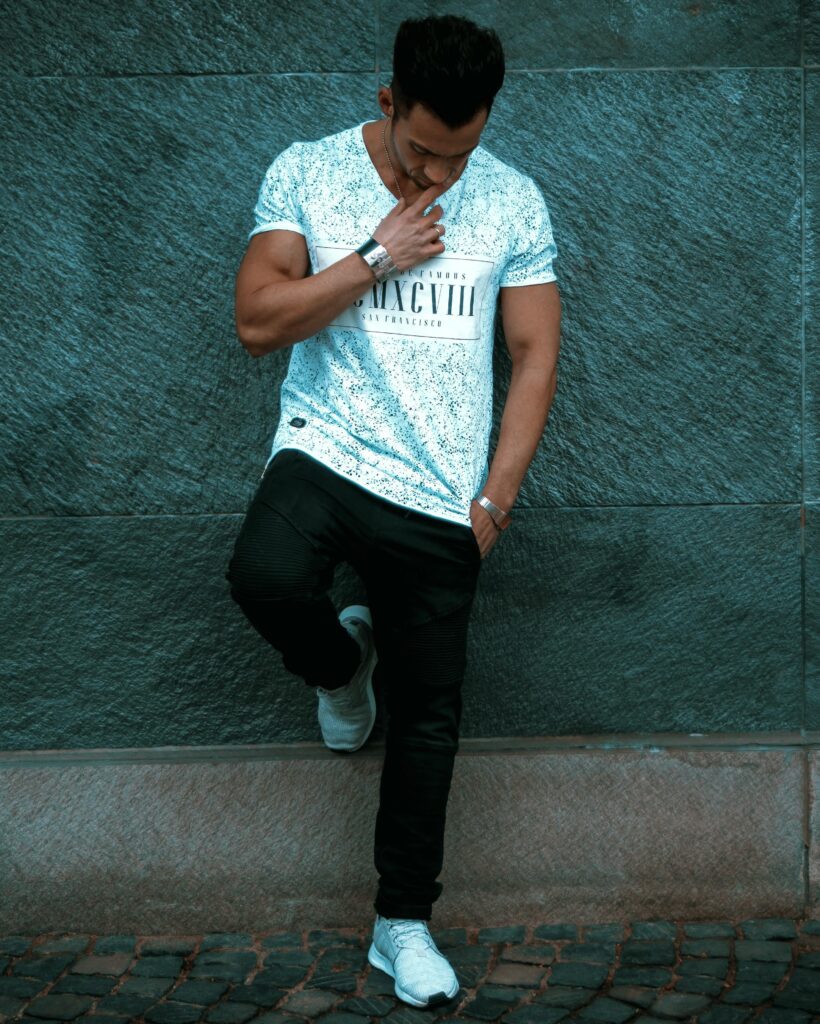 Stylish young man in casual attire leaning against a city wall, exuding a pensive mood.
